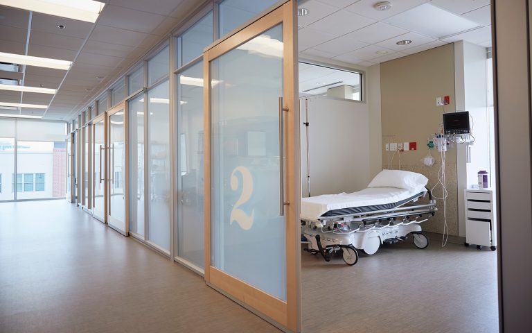 Ein Krankenhauszimmer mit leerem Klinikbett und Beistellschrank, aufgenommen aus dem davor liegenden Flur. Die Qualität von Krankenhäusern soll mit dem neuen Klinik-Atlas besser vergleichbar sein.